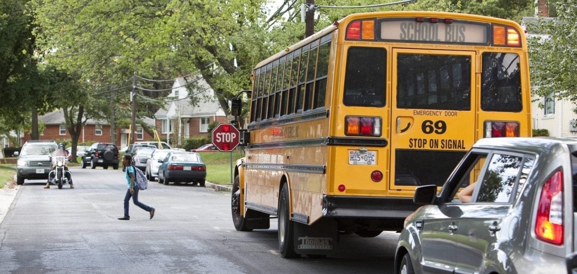 stopped school bus with its stop sign letting child cross the street