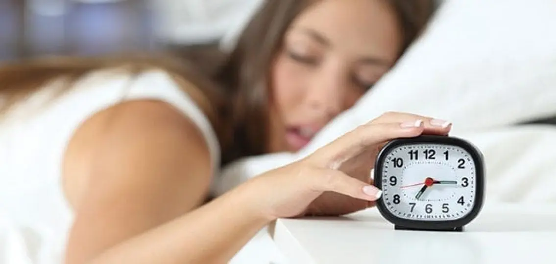 sleeping teenager hitting the snooze button on an alarm clock