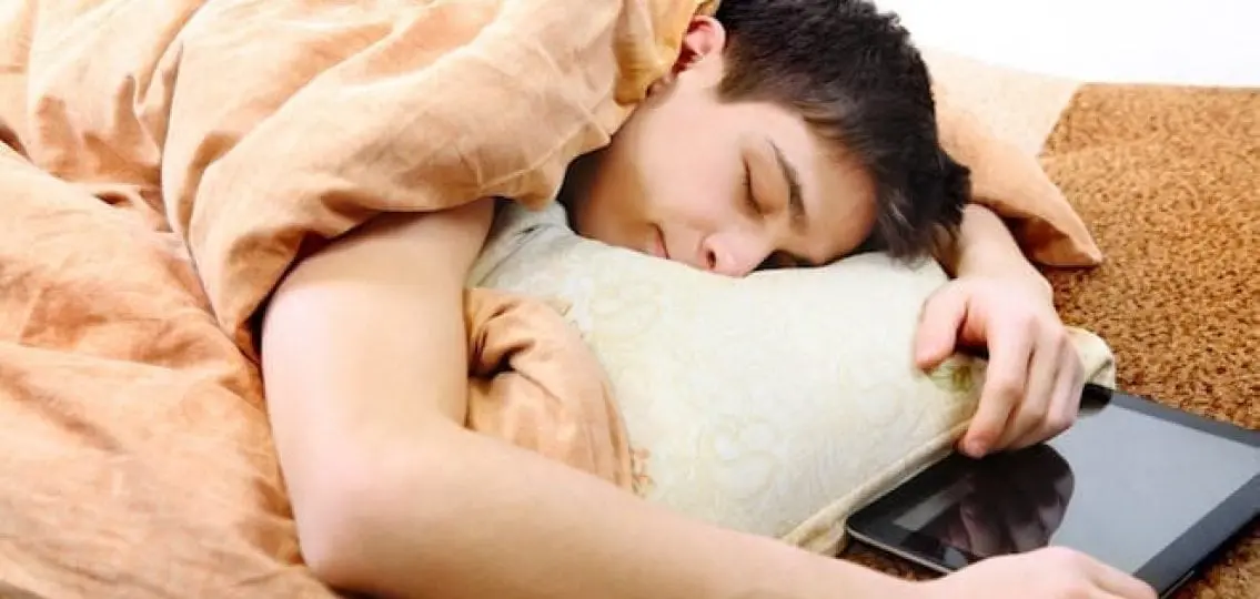 sleeping teenage boy in bed holding an ipad