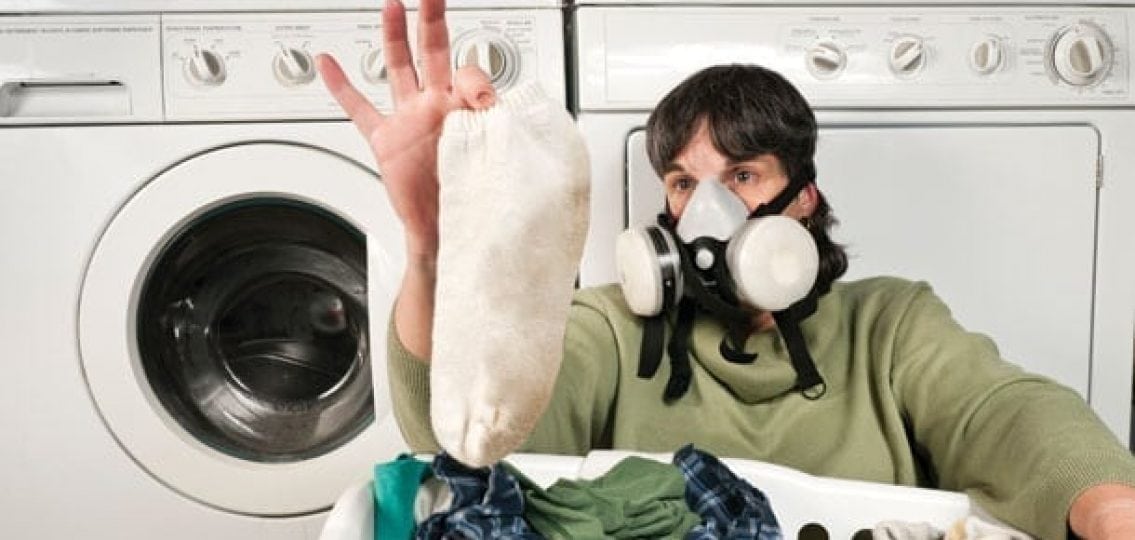 mom in gas mask looking at teen's sock in front of laundry machine