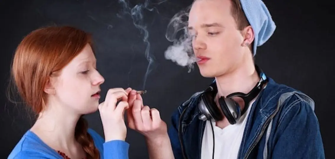 teenagers sharing a joint and breathing out smoke on a black background