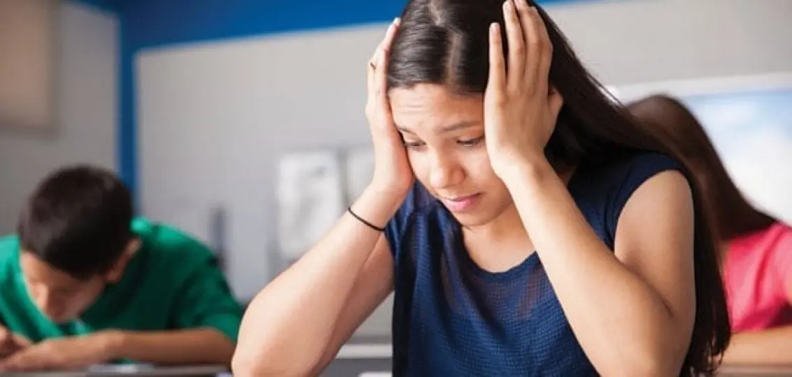 stressed girl taking a test in a classroom with her head in her hands coping with anxiety during test