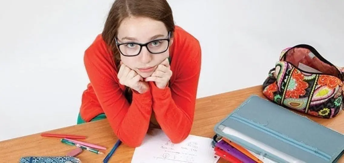 teenage girl leaning on her hands struggling with her homework looking upset at the camera