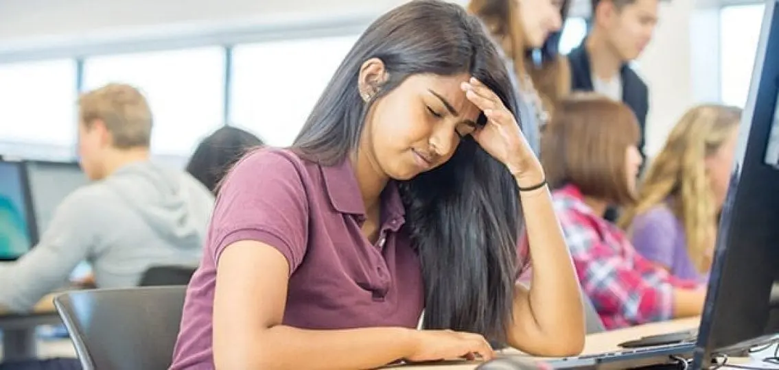 stressed teenage girl at a computer grabbing her head