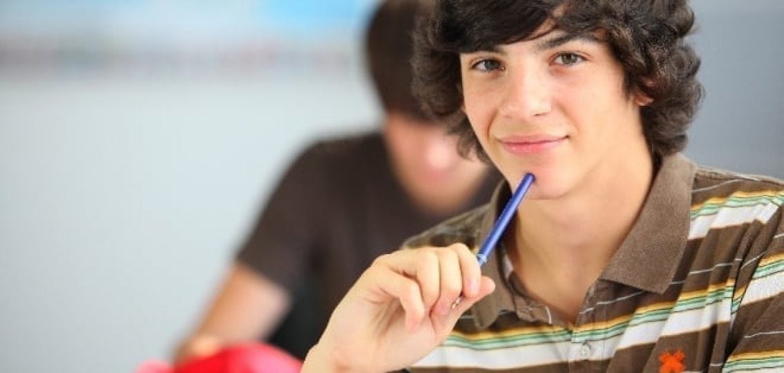 teenage boy in a classroom tapping a pen to his chin