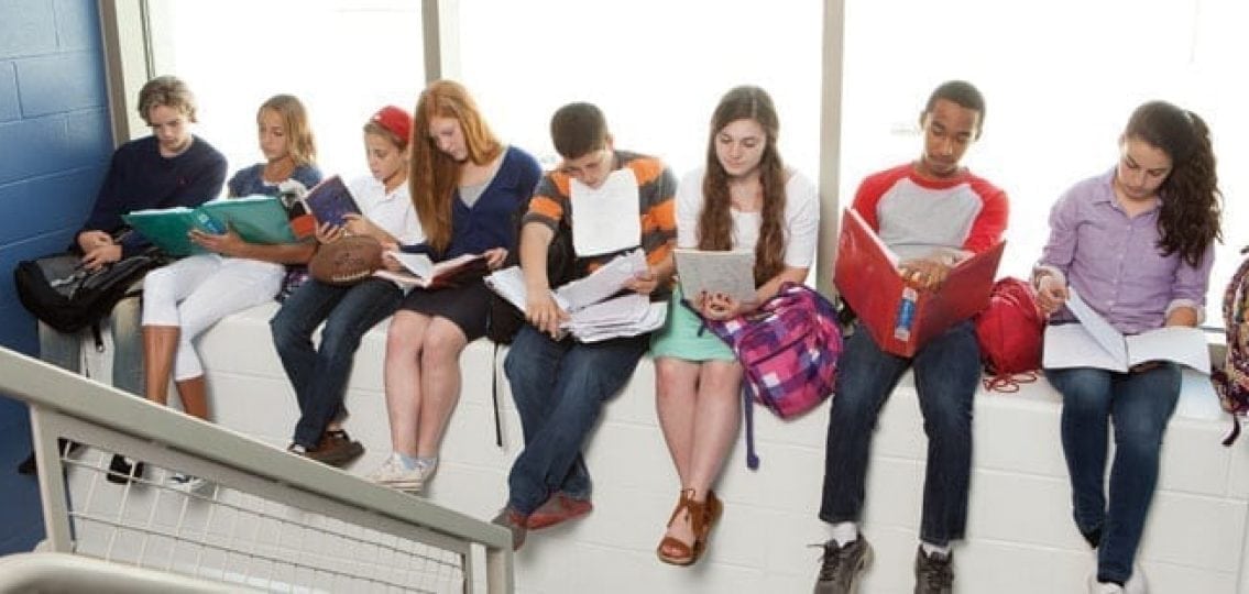 teenagers studying sitting on a window ledge by the stairwell in a school