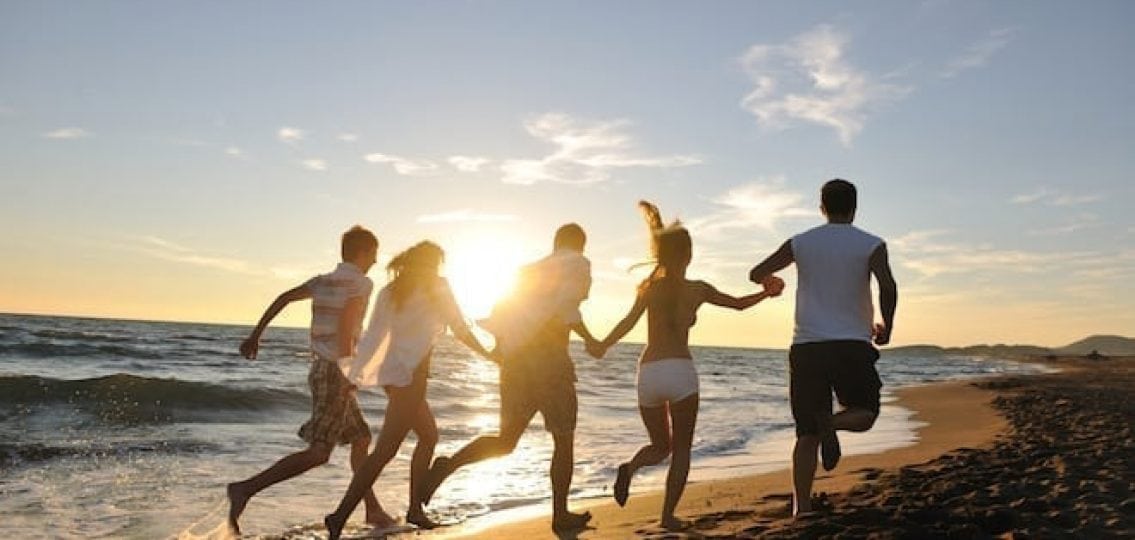 chain of teenagers holding hands and sprinting down the beach at sunset