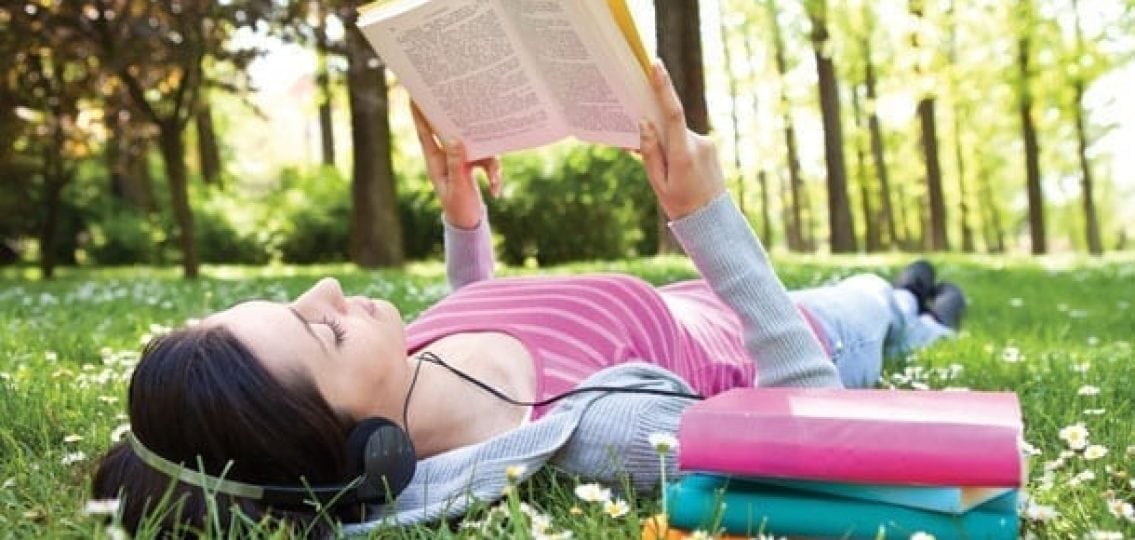 teen reading a book lying in the grass with headphones