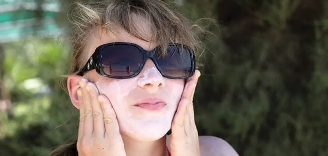 teenager putting on sunscreen outside in sunglasses