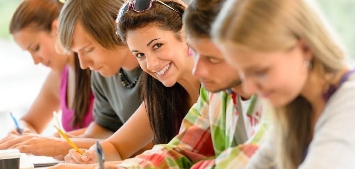 teen girl smiling while other teens do their homework around her