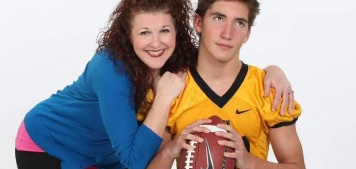 annoyed high school football player with excited mom hugging him