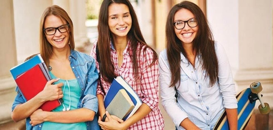 three teen girls holding books and a skateboard
