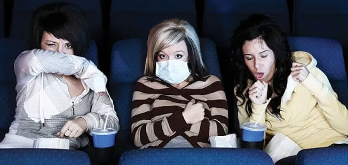 visibly ill teenagers couching and sneezing in a movie theater with a mom in a facemask