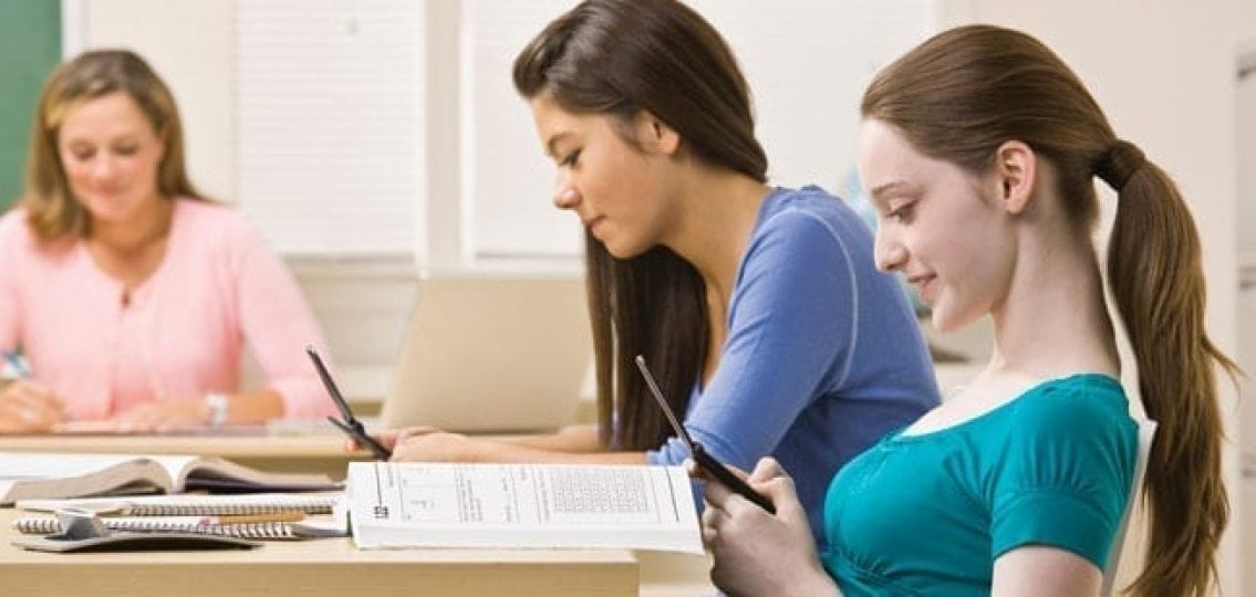 teenage girls texting during class instead of working on their homework