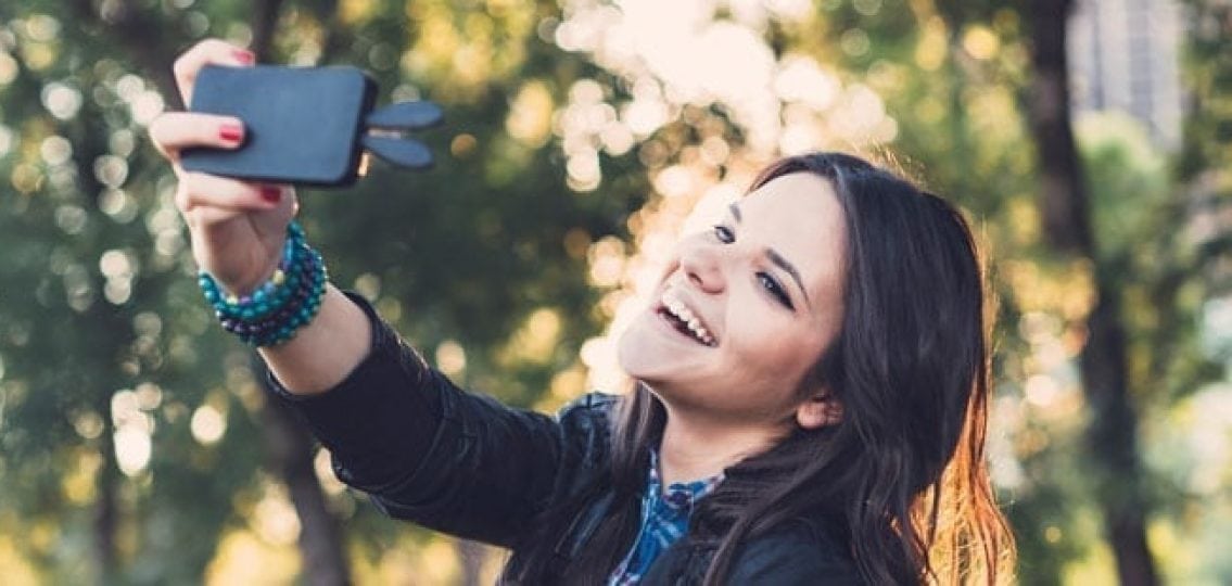 teen girl smiling and taking a selfie outside