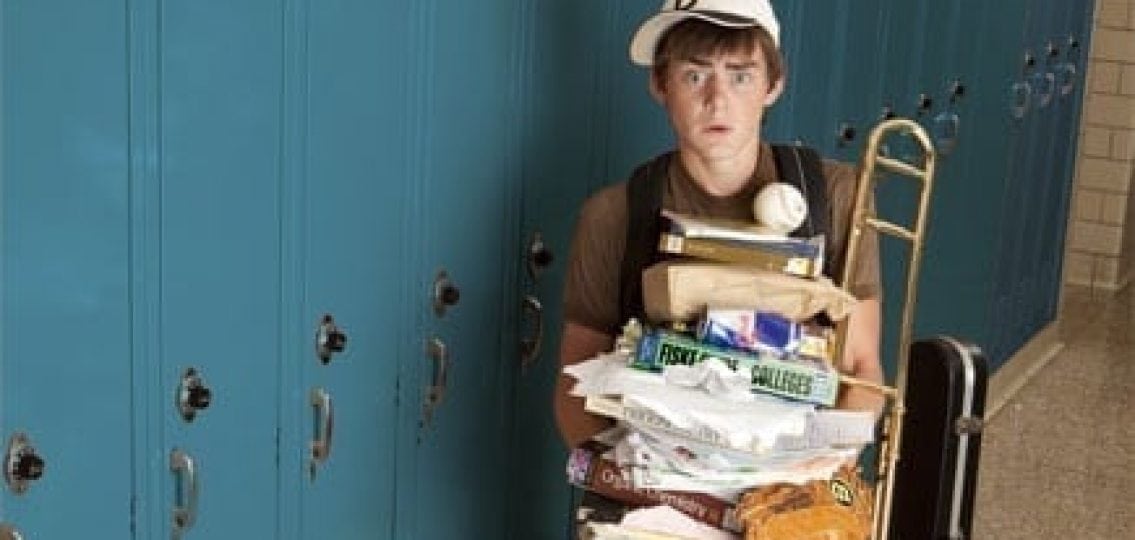 an overwhelmed high school boy with homework and extracurricular materials like baseball equipment and instuments