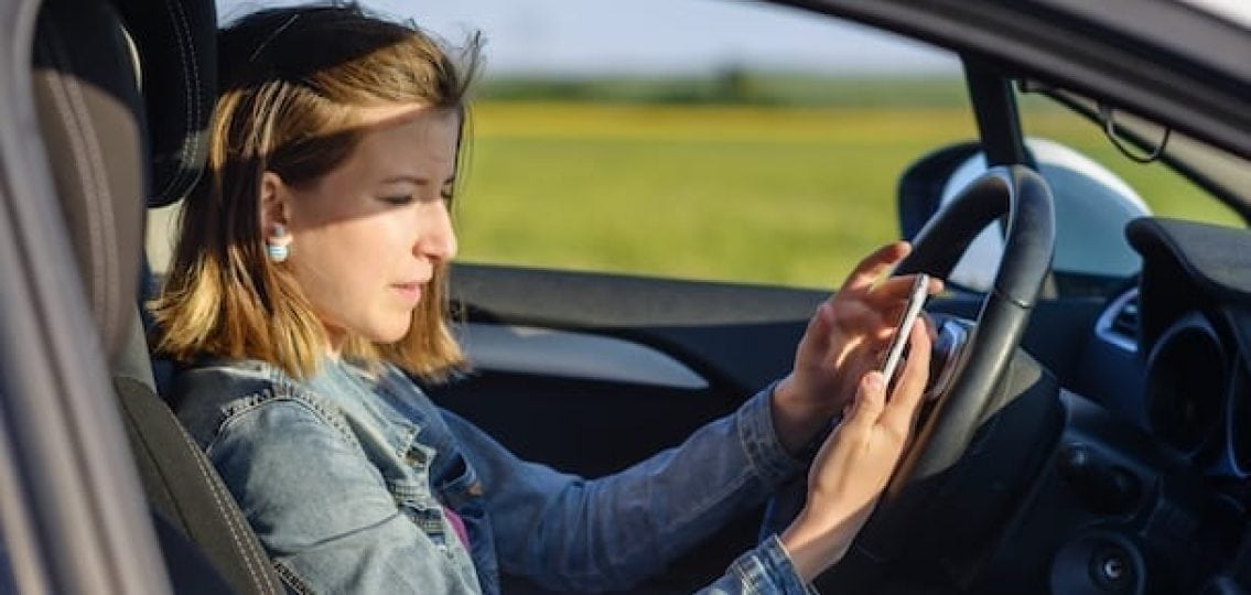 teenage girl texting behind he wheel on a country road