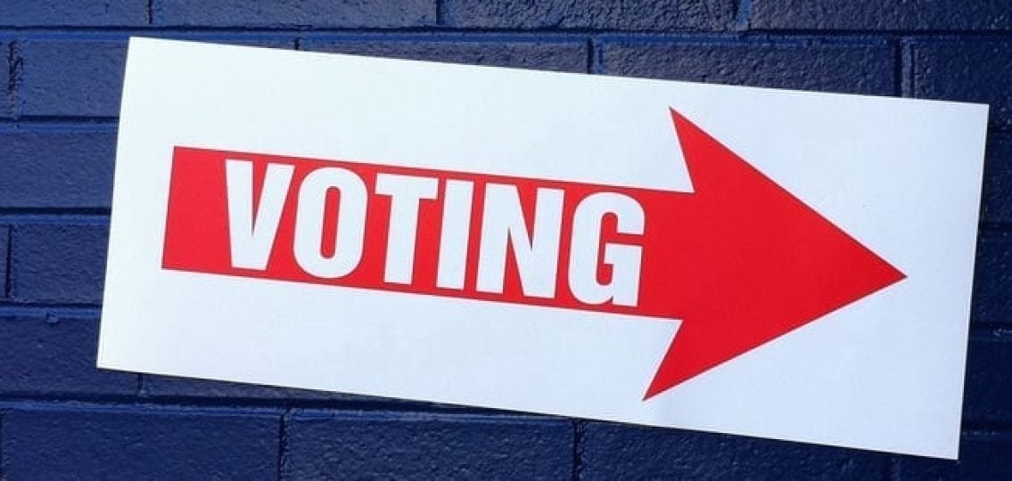 sign on a blue brick wall pointing toward Voting