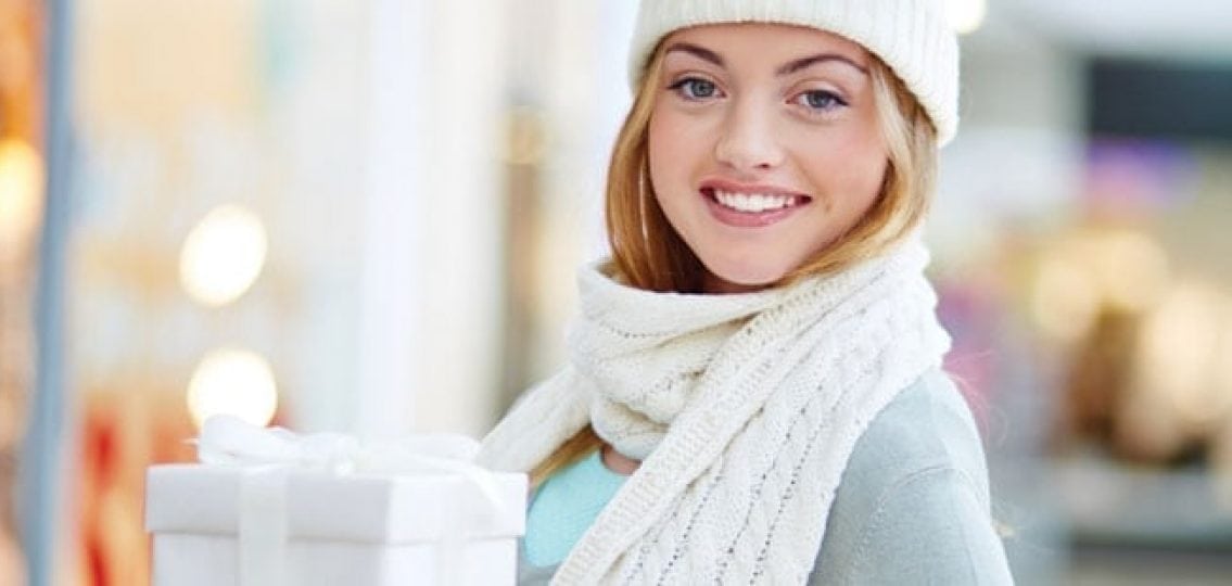 teen girl or young woman in winter coat hat and scarf holding a white present.