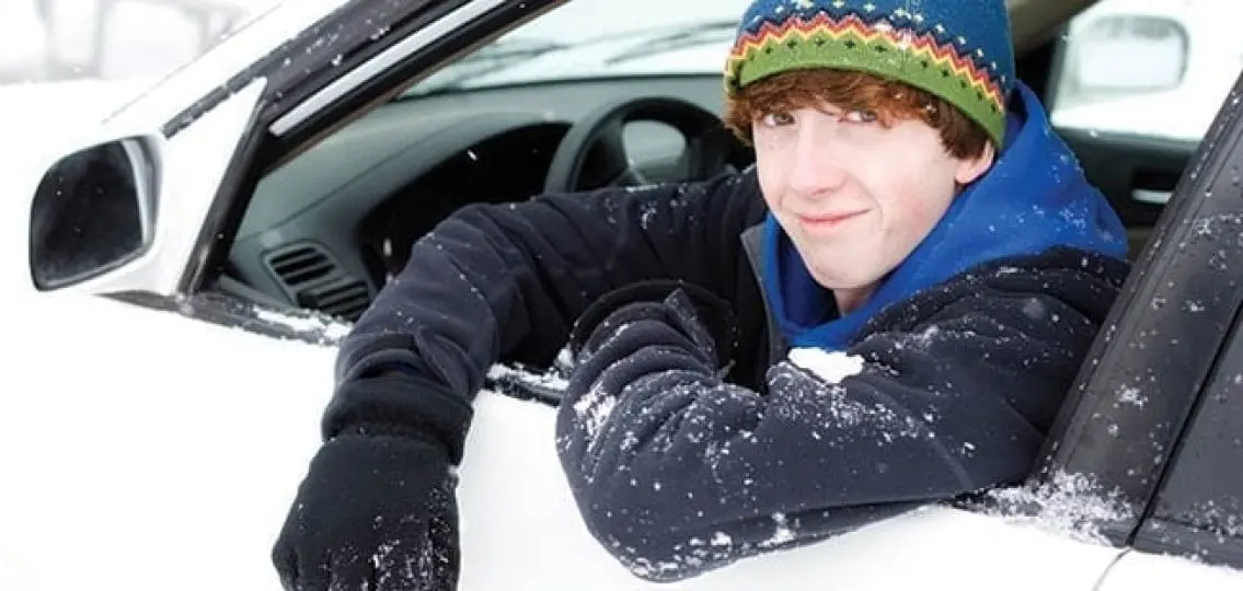 teenage boy hanging out of the car window in winter clothes covered in snow winter driving