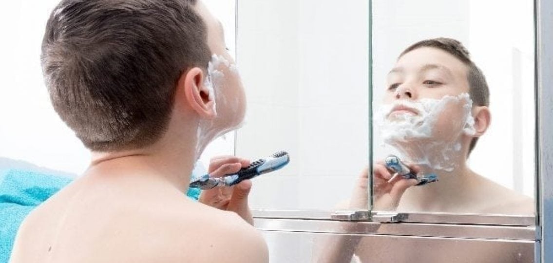 young prepubescent boy with a razor trying to shave in the mirror