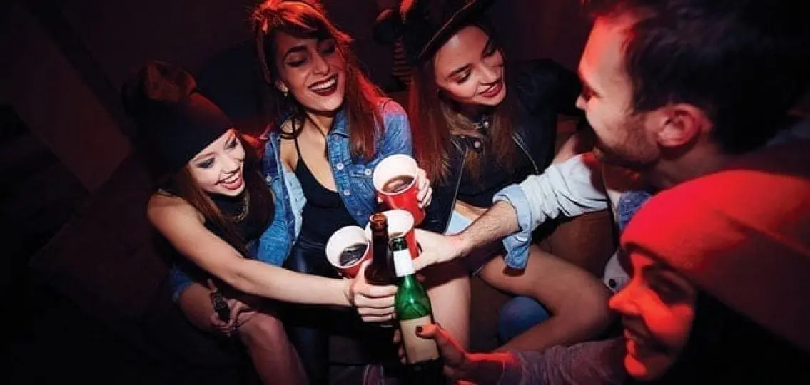 teens under red light at a party with alcohol cheering and drinking