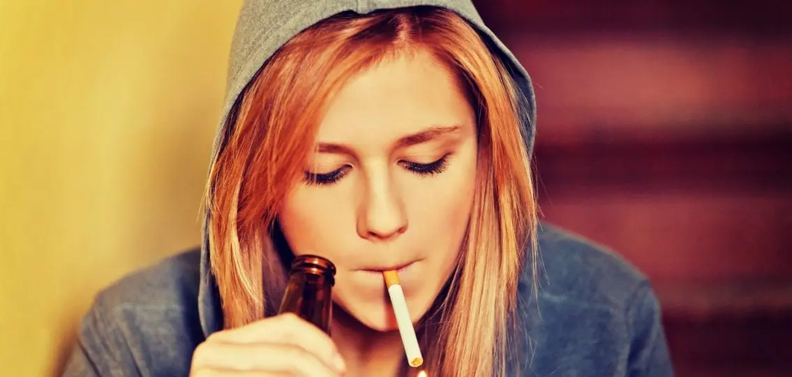 teen girl in hoodie lighting a cigarette holding a beer