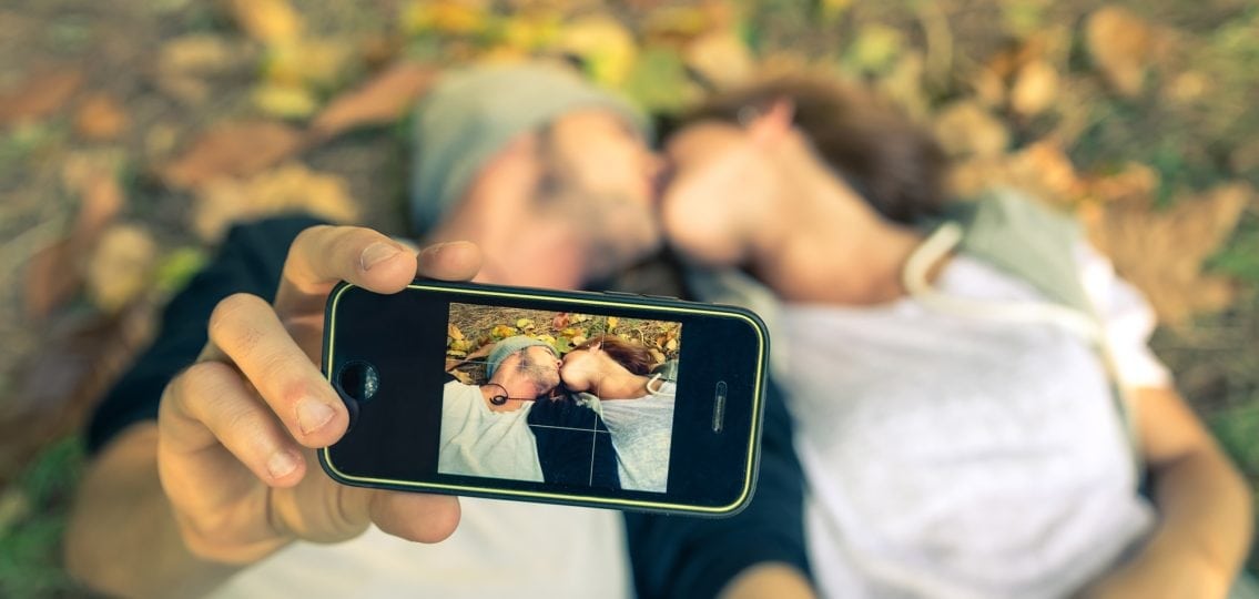 two teenagers kissing in the grass while taking a selfie