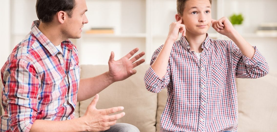 teen boy covering ears rolling eyes ignoring his annoyed father