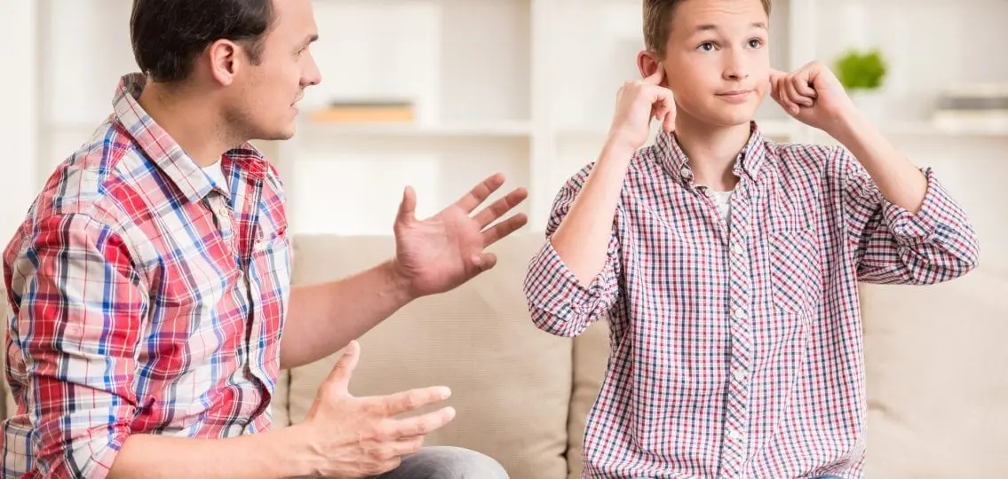 teen boy covering ears rolling eyes ignoring his annoyed father