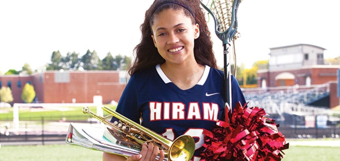 college girl in a hiram jersey holding a lacrosse stick a trumpet and books