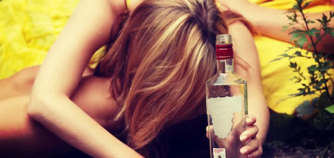 drunk unconscious girl slumped over on the dirt with a bottle of vodka