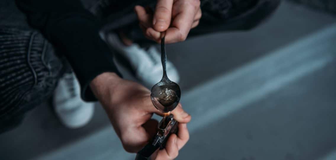 a heroin addict lighting a lighter under a spoon