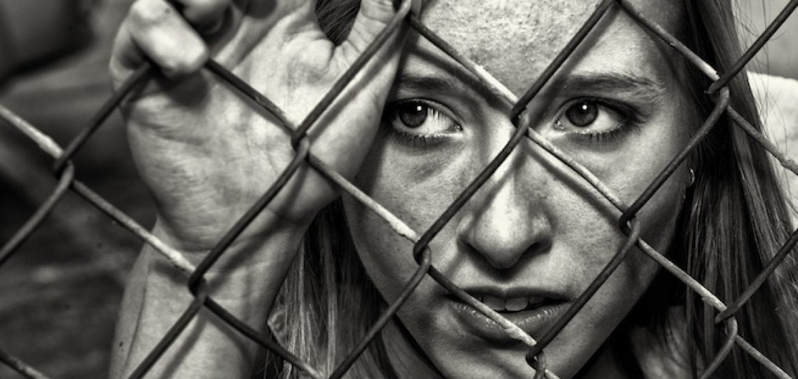 teen girl in black and white behind a chainlink fence