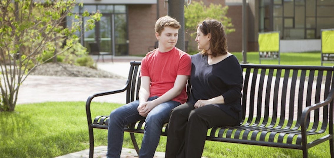 mom and teenage boy sitting on an outdoor bench and talking