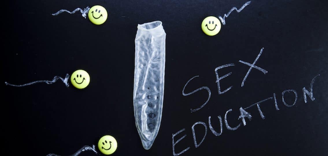 chalk board with images of smilie faces with tails to represent sperm moving toward an empty condom with the word Sex Education