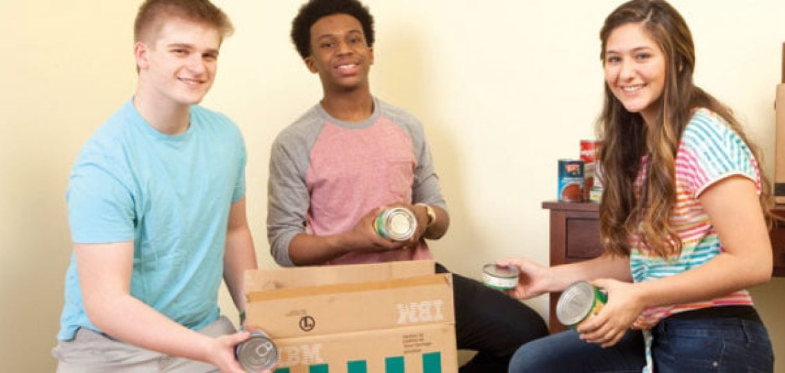 teens volunteering and packing canned food into cardboard boxes