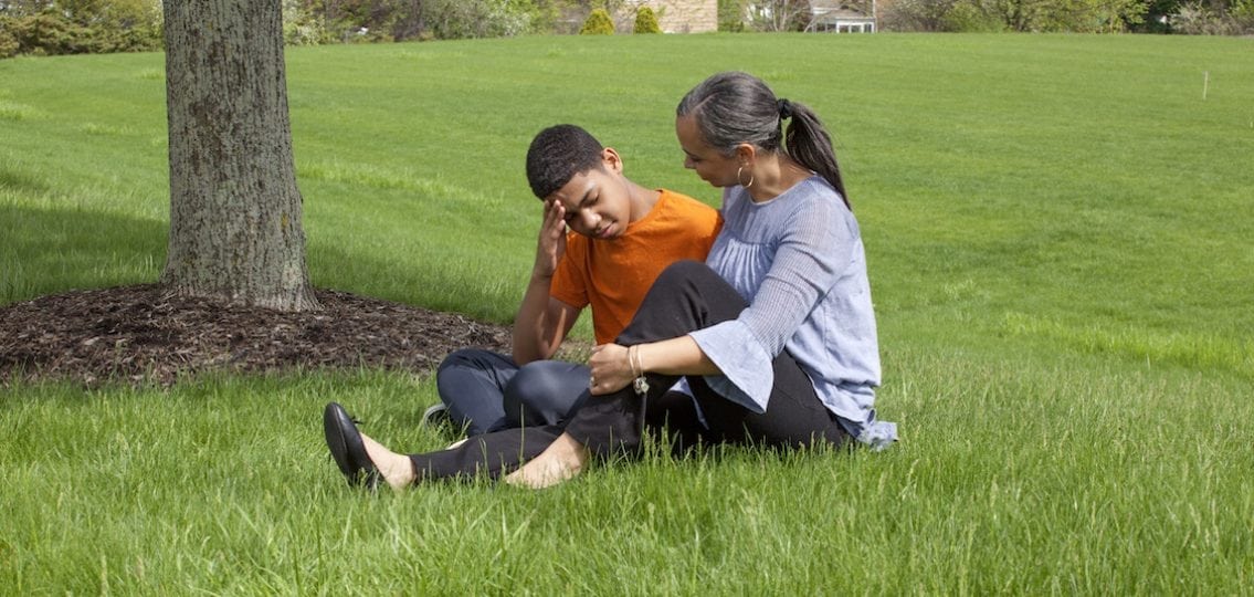 mom comforting sad son sitting in the grass outside