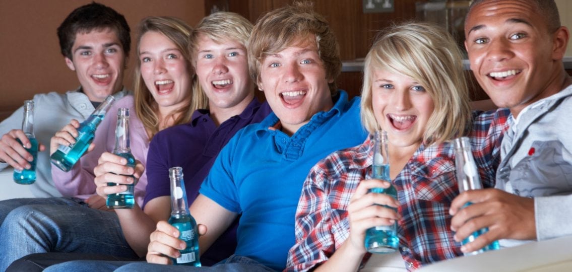 Teens hanging on a sofa in the basement drinking blue soda