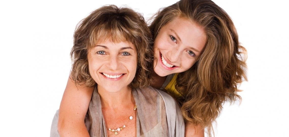 teen daughter hugging her smiling mom from behind