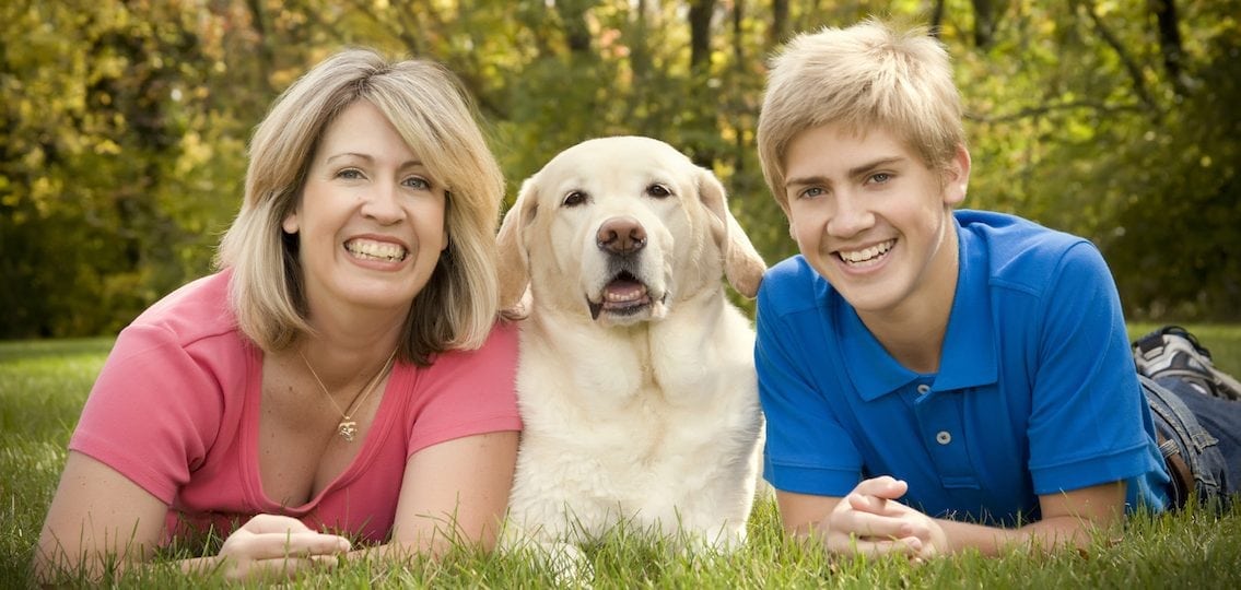 mom and teen son next to a yellow lab in the grass