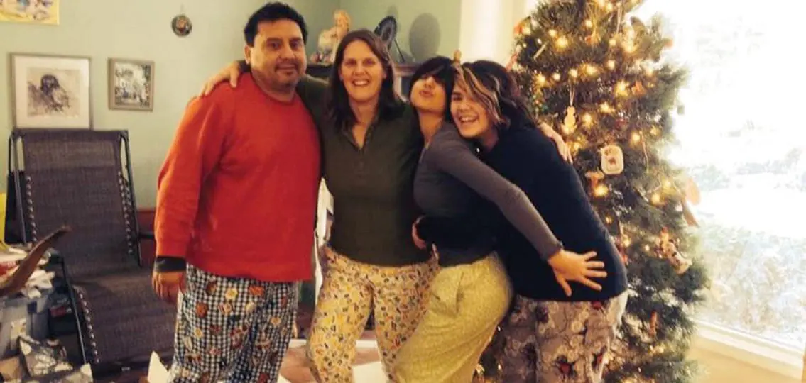 family in pajamas posing and laughing in living room in front of christmas tree