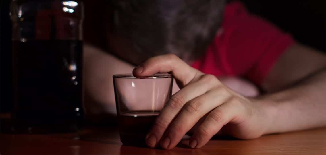 drunk person lying facedown on a table behind a shotglass