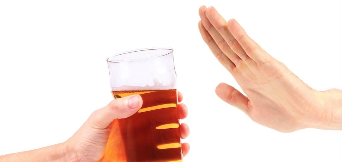 a hand saying no to a glass of beer