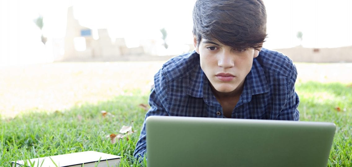 boy writing college essay on a laptop outside