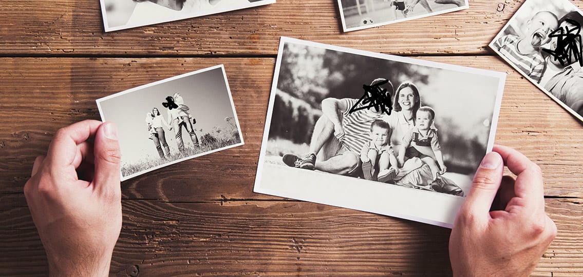 Black and white family photos laid on a table with one face crossed out in each picture