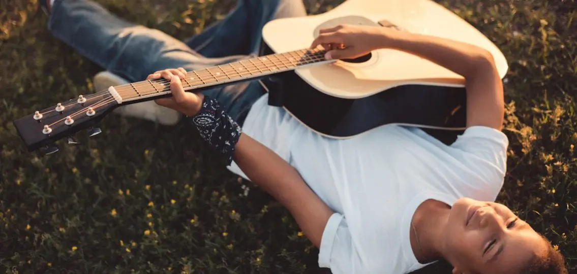 teen playing the guitar lying on the grass