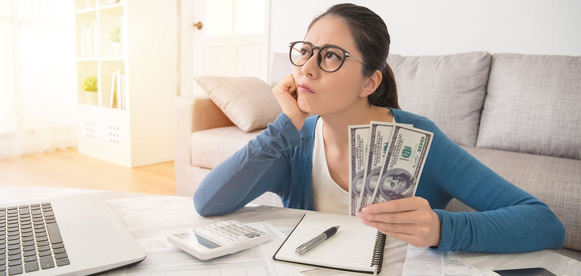 teen girl or young woman holding three hundred dollars calculating budget in frustration