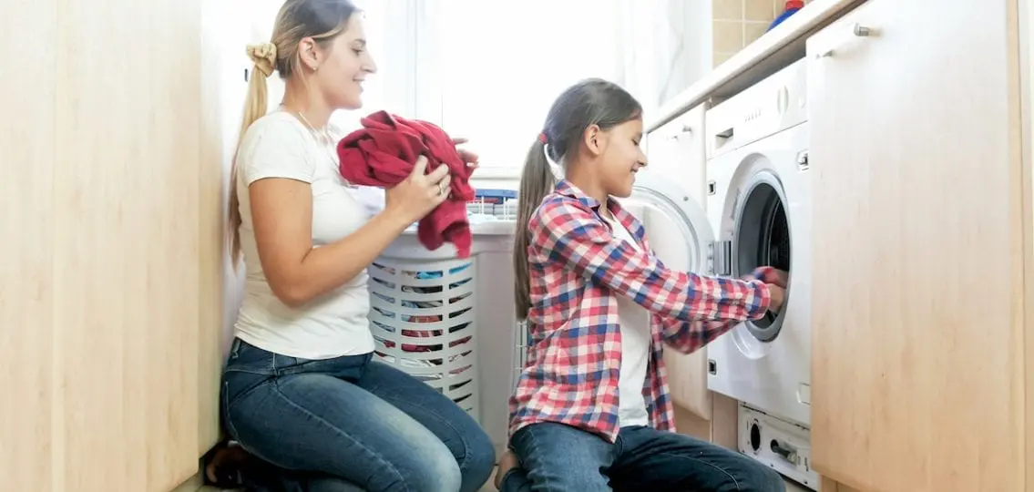 Smiling Teenage Girl Helping Mother In Laundry Room