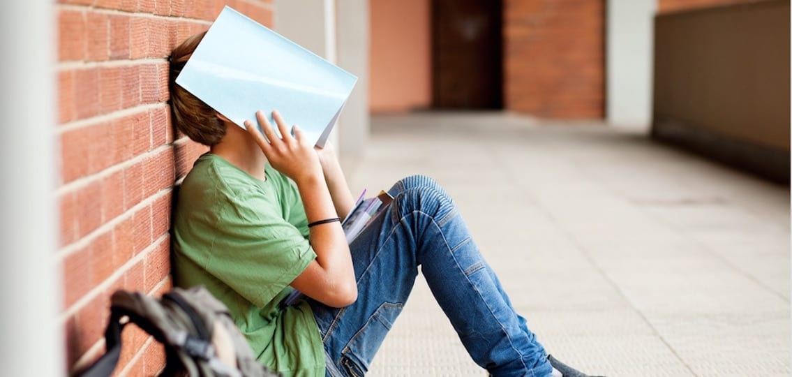 Tired Teen Leaning On Wall At School and covering face with a folder